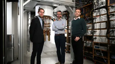 Three people in a laboratory with large technical equipment, visible cables and electronics racks.